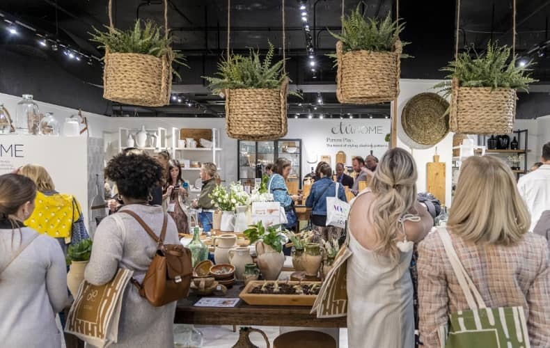 Various people are gathered in a showroom. There are plants hanging from the ceiling, and plants scattered around the space.